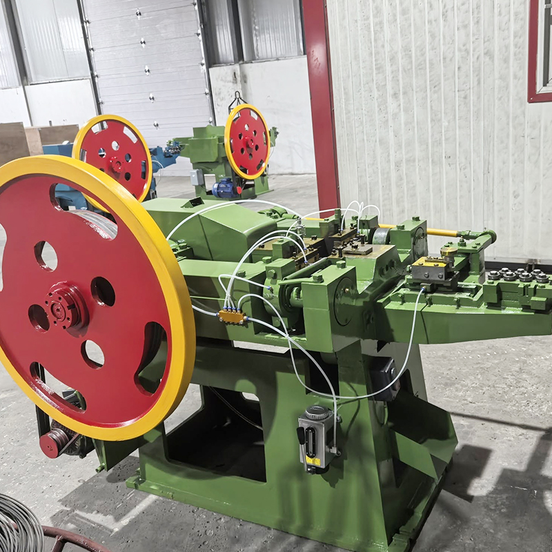 713 Nail Making Machine - YF Metal Tech Green Industrial Machine with Large Red and Yellow Flywheels in a Workshop Connected by White Wires and Metal Components