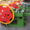 Row of green industrial machines with large red flywheels with yellow rims in a factory setting.